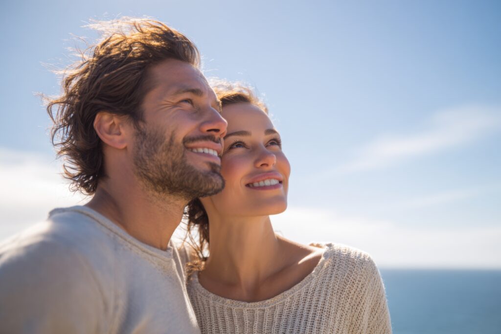 Pareja feliz sonriendo y mirando al cielo junto al mar.